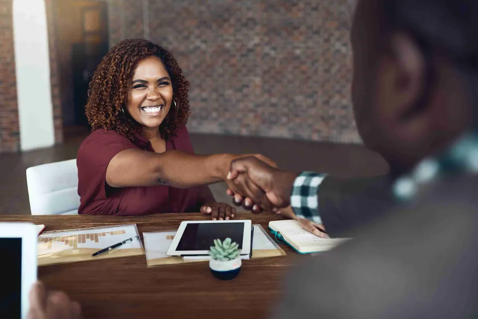 Smiling woman shaking hands across a desk